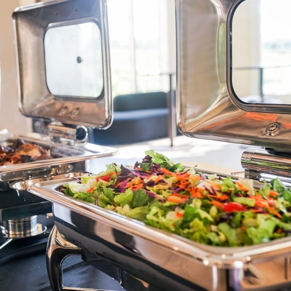 A vibrant salad with mixed greens, shredded carrots, and red cabbage in a Guapo's buffet chafing dish.