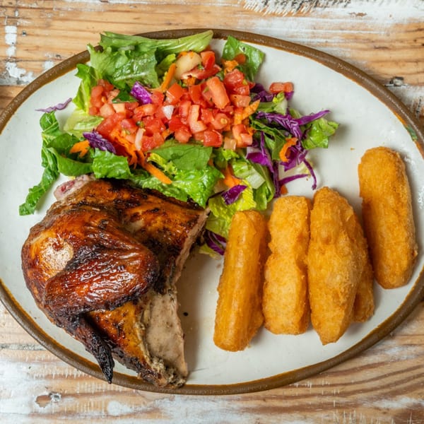 Guapo's GO charcoal chicken with crispy skin, fresh salad, and golden fried yuca on a white plate.