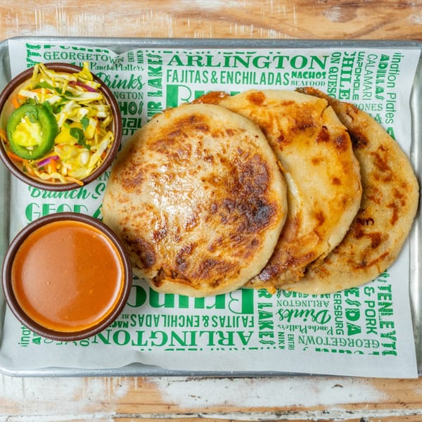 Three pupusas, a bowl of slaw with jalapeños, and a bowl of red sauce on a tray.