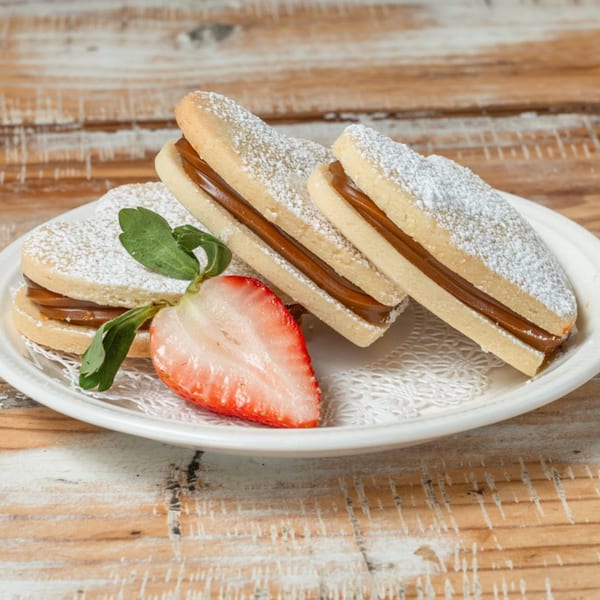 Three alfajores with dulce de leche filling, powdered sugar, and a strawberry half on a white plate.