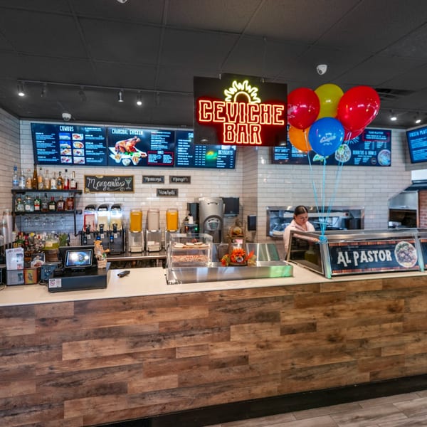 Guapo's GO counter with a neon "Ceviche Bar" sign, menu boards, drinks, and a staff member.