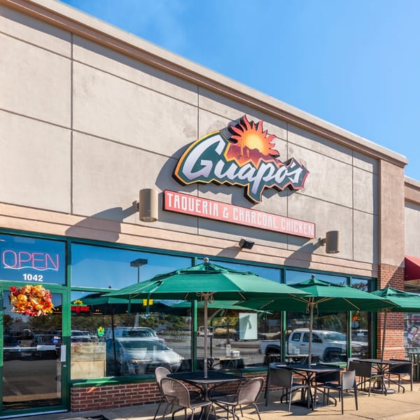 Exterior of Guapo's Taquería & Charcoal Chicken with outdoor seating under green umbrellas.