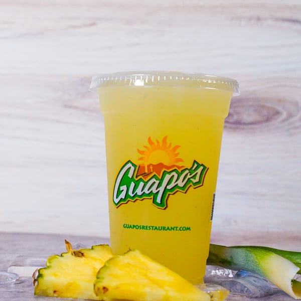 Guapo's pineapple agua fresca in a clear cup with pineapple slices and ice.