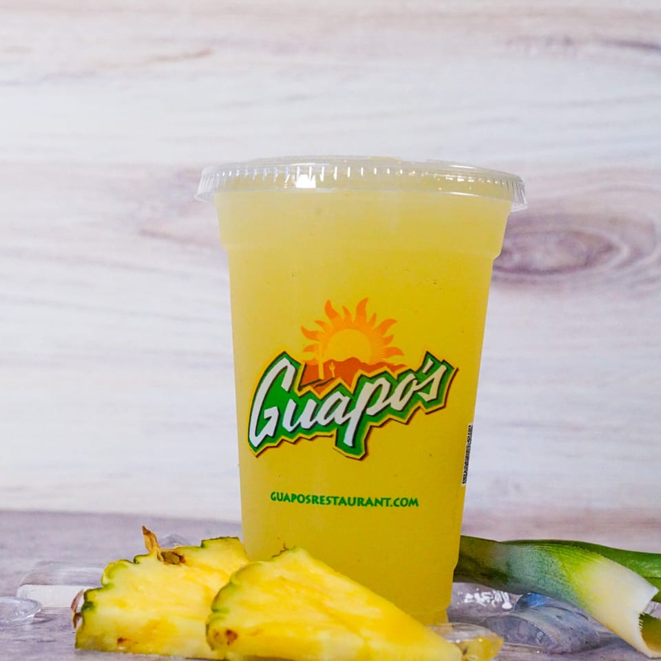 Guapo's pineapple agua fresca in a clear cup with pineapple slices and ice on a wooden surface.