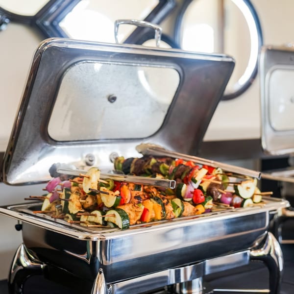 Chicken and vegetable skewers, including zucchini, bell peppers, and red onion, in a chafing dish.