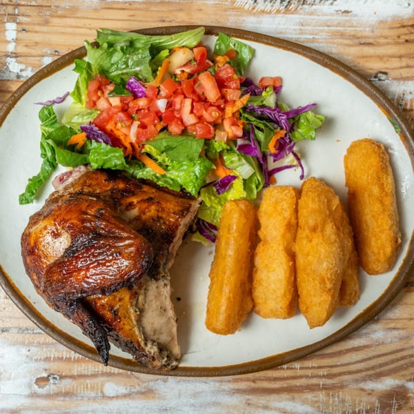 Guapo's GO charcoal chicken with a side salad and golden fried yuca on a white plate.