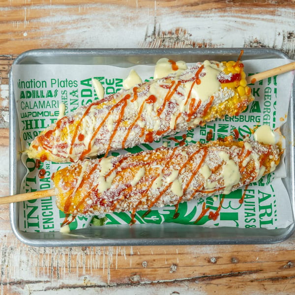 Two Guapo's GO elotes, grilled corn on the cob, topped with cheese, sauce, and chili powder.