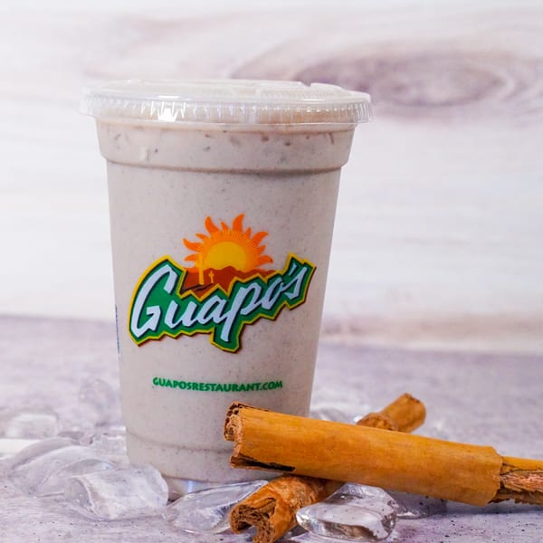 Guapo's horchata drink in a plastic cup with ice and cinnamon sticks on a light background.