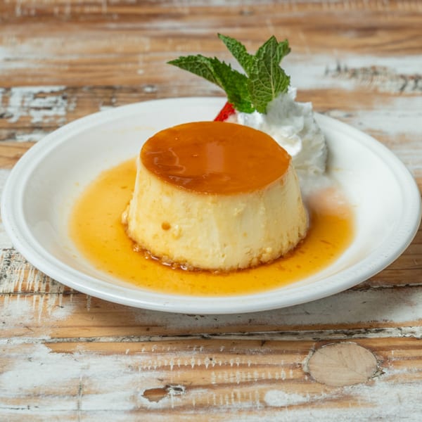 Flan dessert with caramel sauce, whipped cream, and a mint sprig on a white plate.