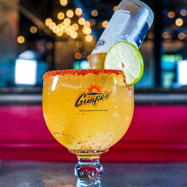Guapo's Michelada with a Corona beer bottle, lime, and chili-salted rim, against a blurred background.