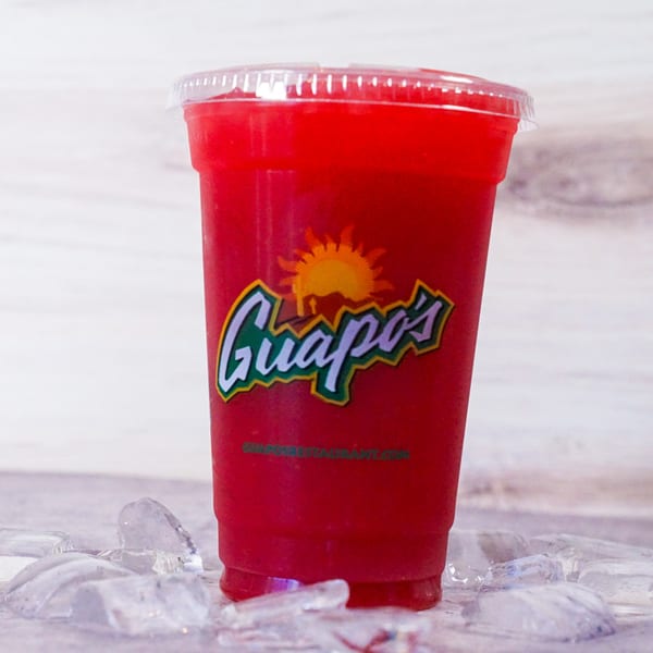 A red Guapo's GO frozen drink in a clear plastic cup, surrounded by ice cubes.