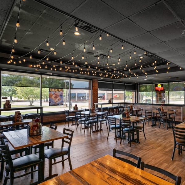 The spacious dining area of Guapo's GO features wooden tables, black chairs, and string lights overhead.