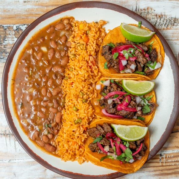 Three Guapo's GO steak tacos with lime, rice, and charro beans on a white plate.