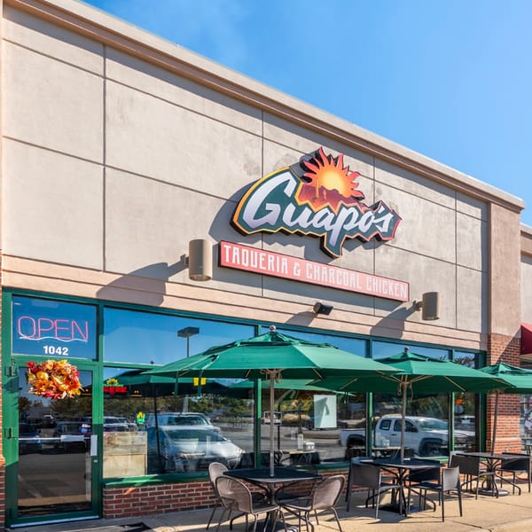 Exterior of Guapo's Taquería & Charcoal Chicken with outdoor seating under green umbrellas.