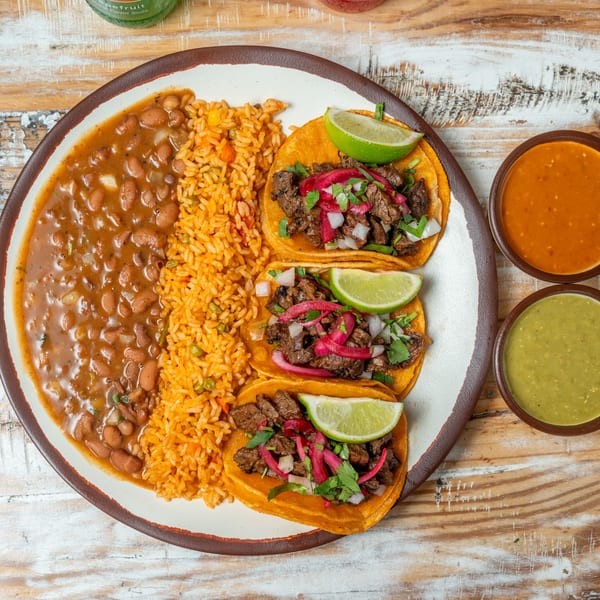 Three Guapo's GO tacos with rice, beans, and two bowls of salsa on a rustic wooden table.