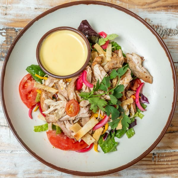 Guapo's GO charcoal chicken salad with tomatoes, pickled onions, tortilla strips, and a side of dressing.